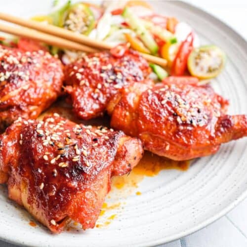 A plate of Korean Gochujang Chicken and chopsticks with salad on the side.
