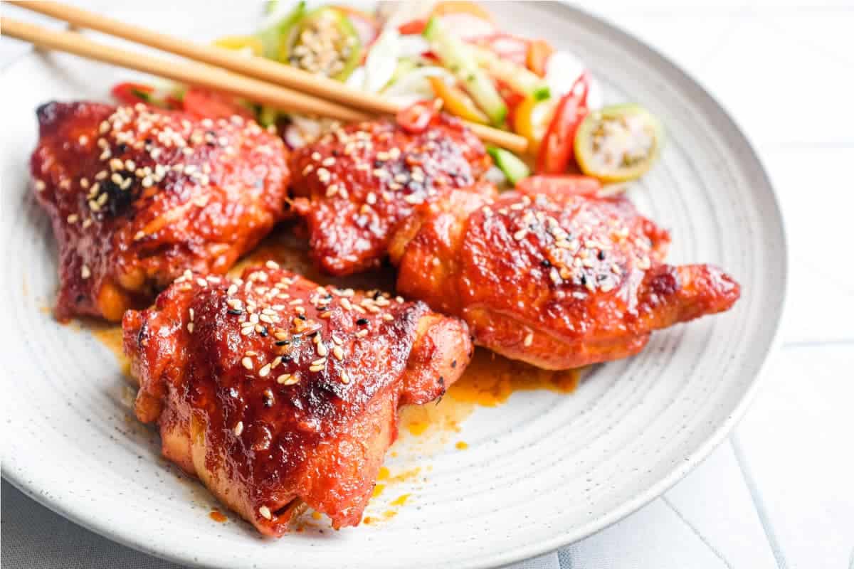 A plate of Korean Gochujang Chicken and chopsticks with salad on the side.