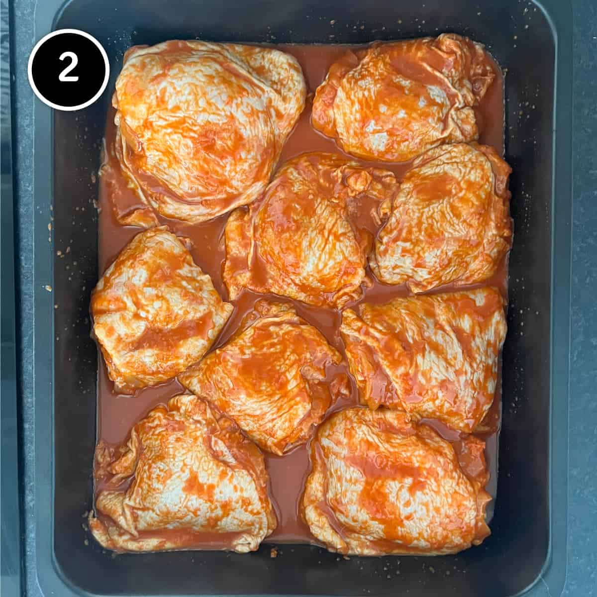 Placing the marinated gochujang chicken in a roasting tin.