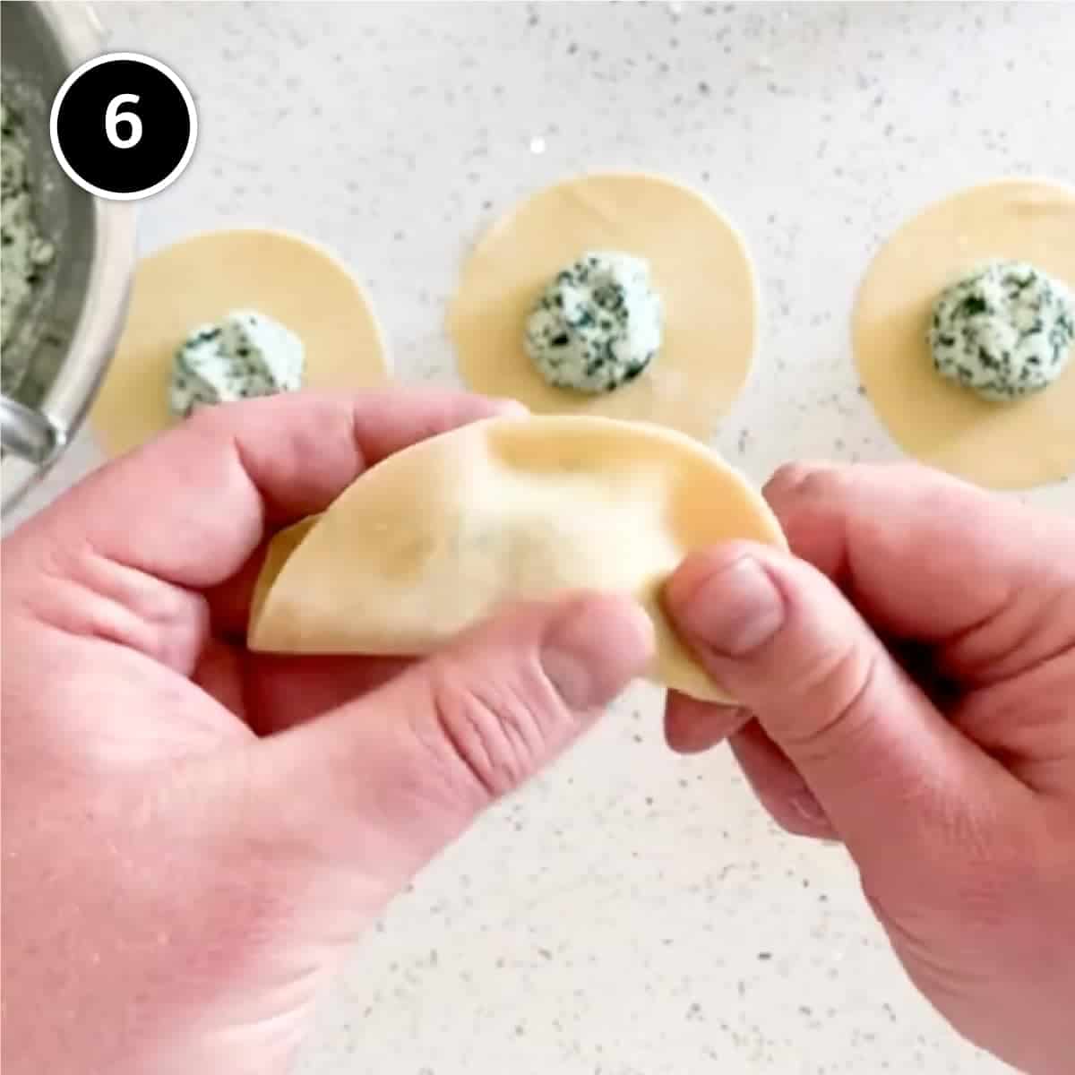 Folding a disc of pasta into a half moon shape.
