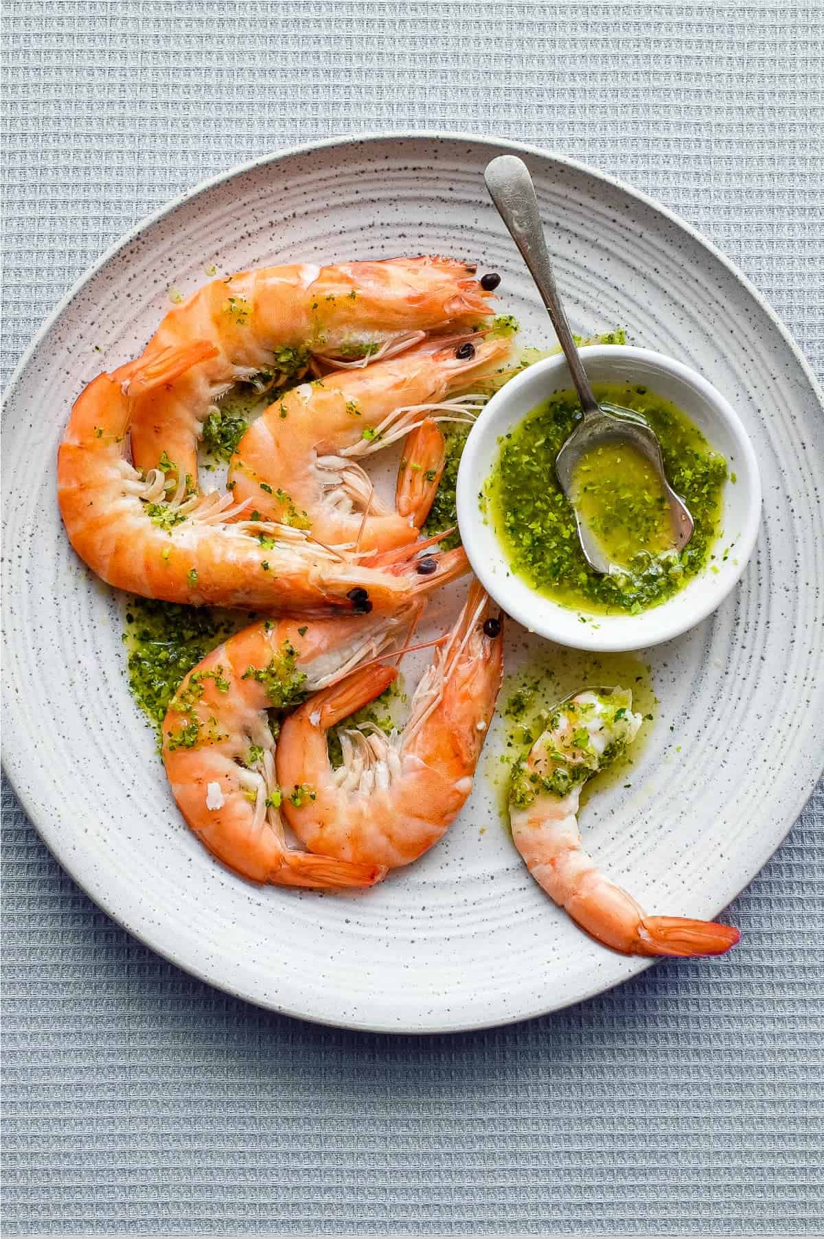 A platter of King Prawns with a small bowl of Italian Salmoriglio sauce, a herb and lemon dressing. A small spoon sits in the bowl.