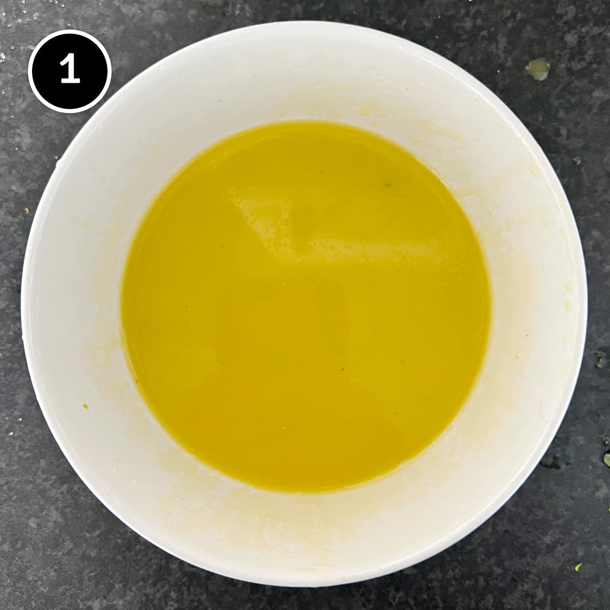 A small bowl holding lemon juice and olive oil, which has been whisked into a light emulsification