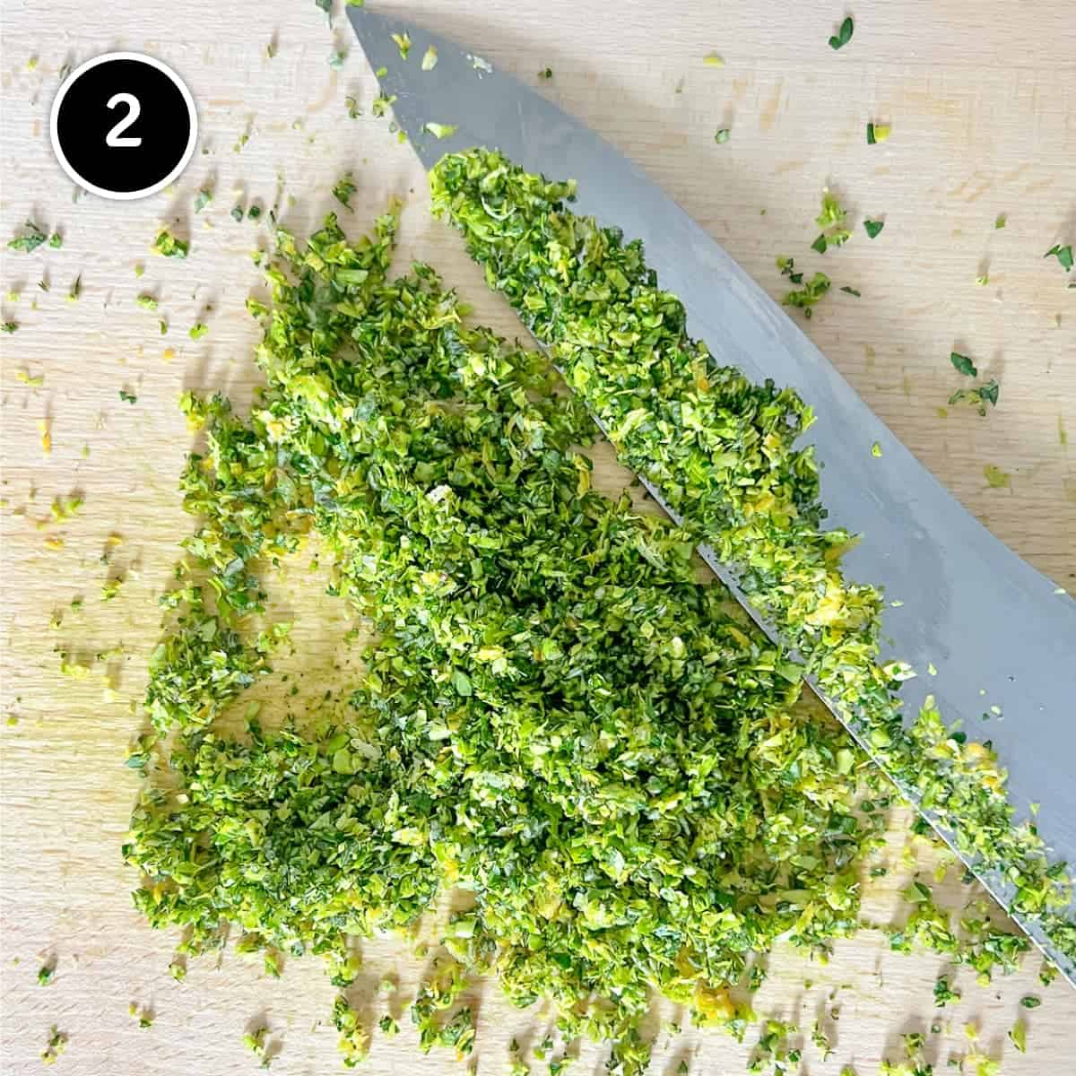 A kitchen knife sits alongside some finely chopped herbs.