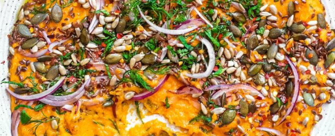 A platter of Turkish carrot salad scattered with herbs, seeds and red onion