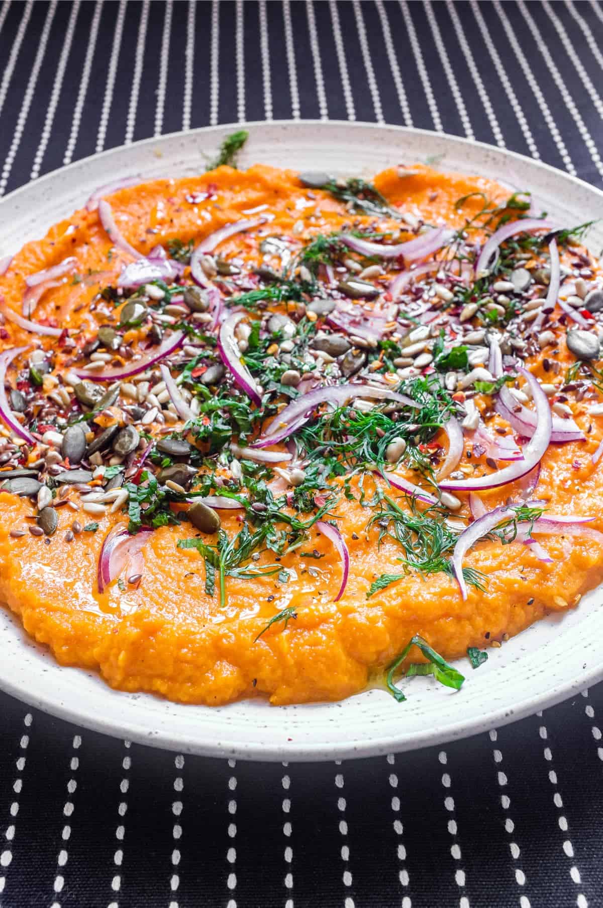 A platter of Turkish carrot salad scattered with herbs, seeds and red onion