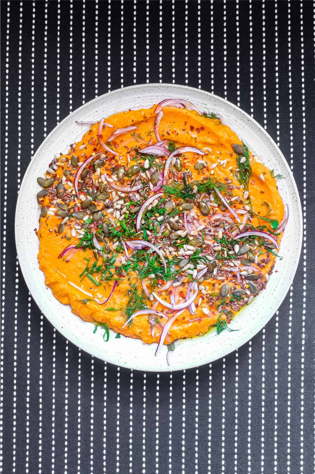 A platter of Turkish carrot salad scattered with herbs, seeds and red onion