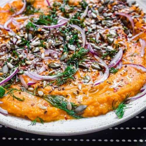 A platter of Turkish carrot salad scattered with herbs, seeds and red onion