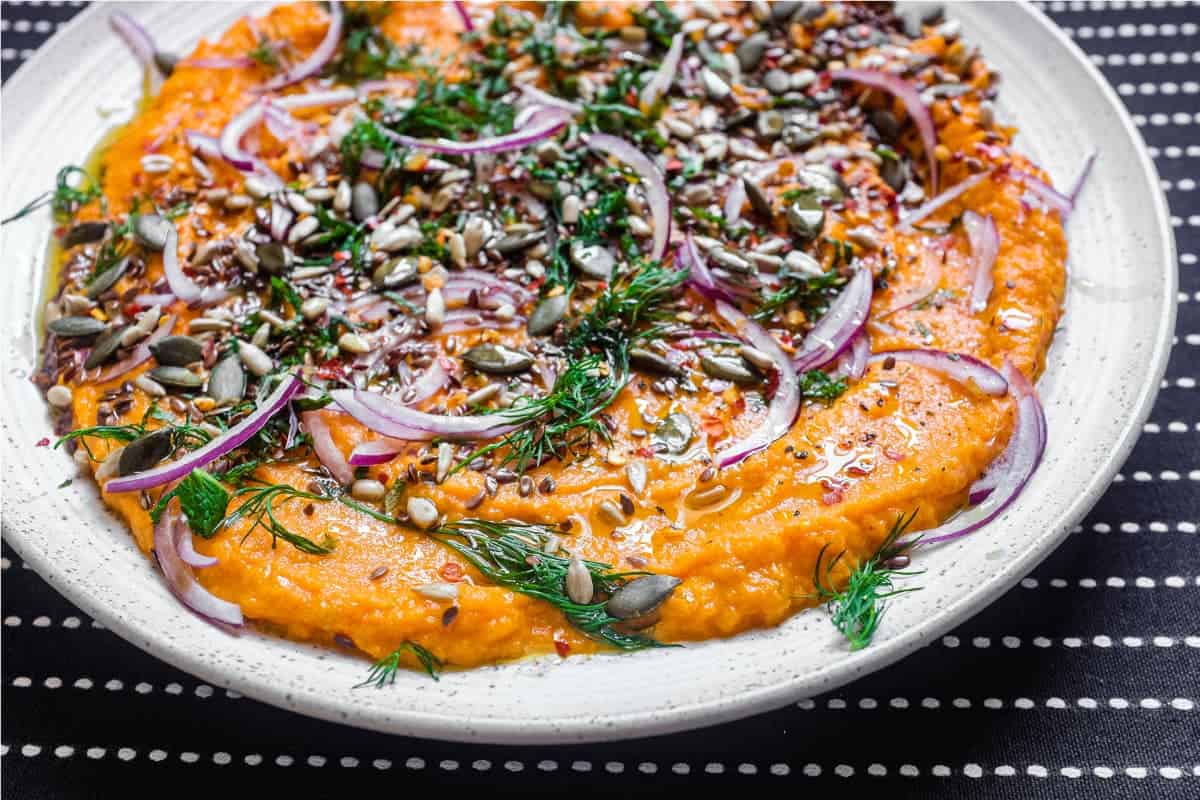 A platter of Turkish carrot salad scattered with herbs, seeds and red onion