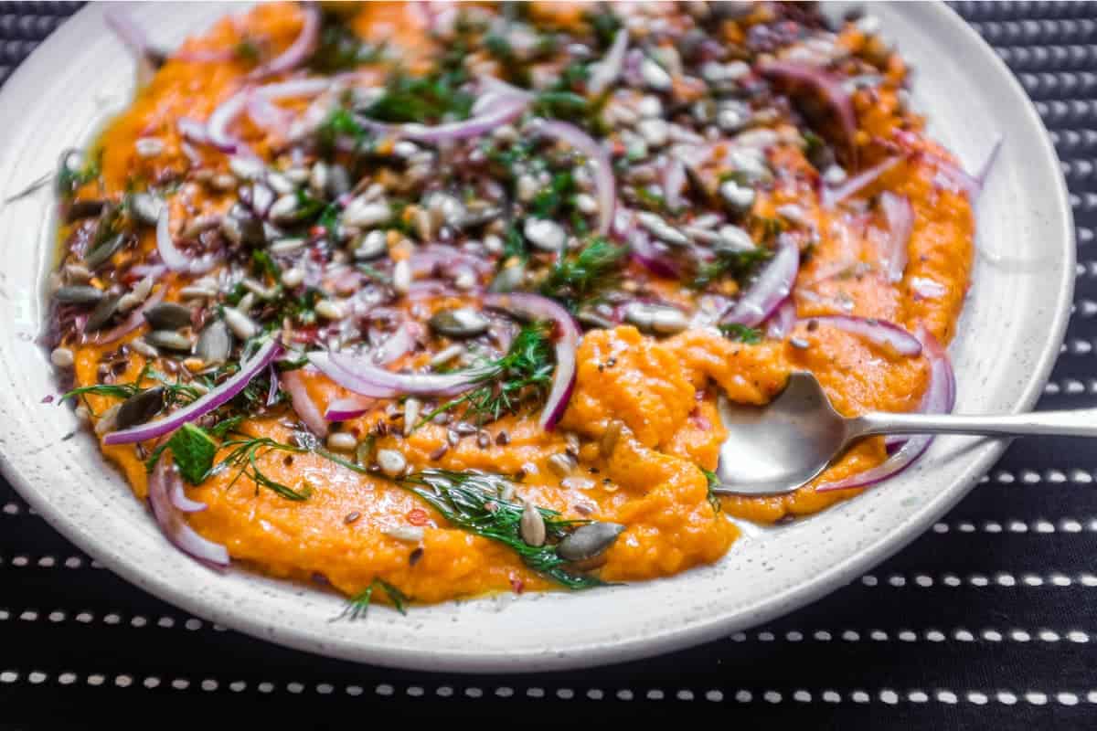 A platter of Turkish carrot salad scattered with herbs, seeds and red onion