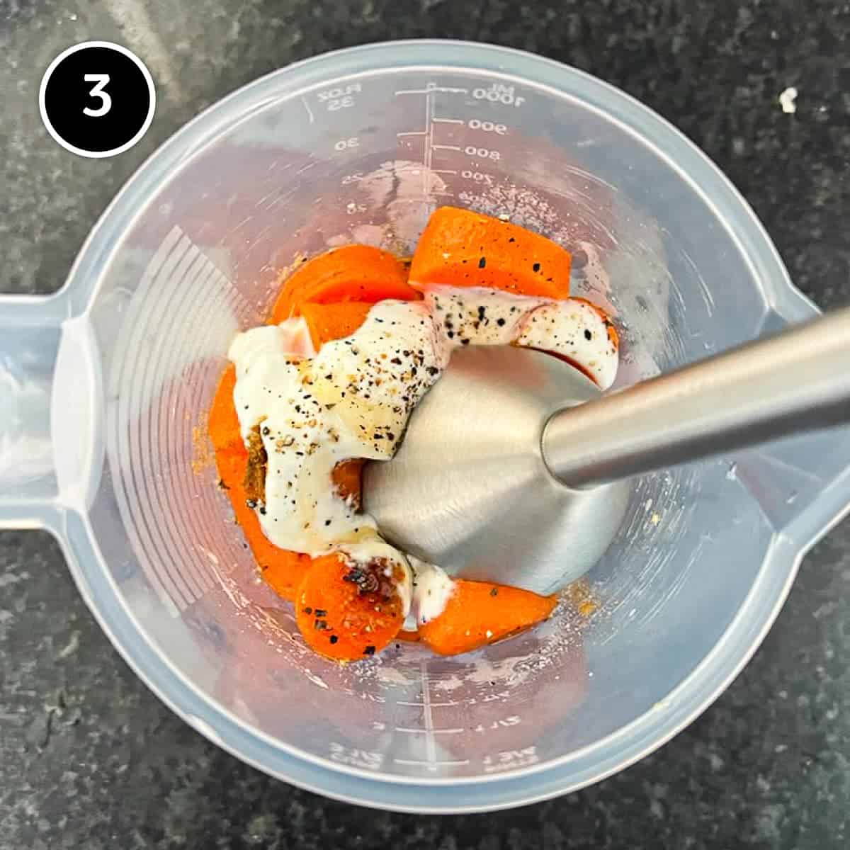 Carrots and yoghurt with spices in a plastic jug, about to be blended by a stick blender