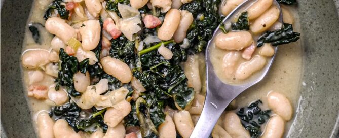A bowl of Tuscan Beans with pancetta and cavolo nero cabbage in a bowl with a spoon