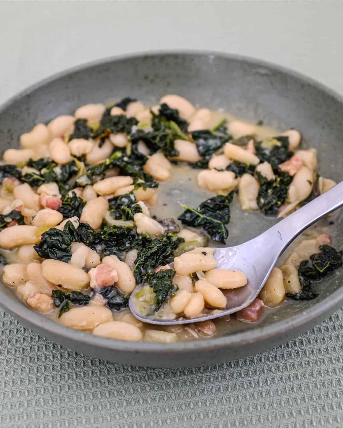 A bowl of Tuscan Beans with pancetta and cavolo nero cabbage in a bowl with a spoon