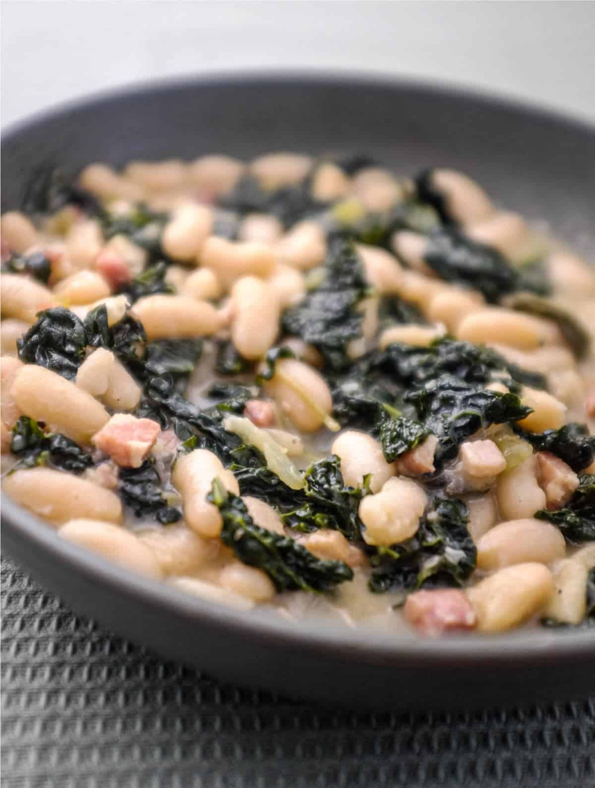A bowl of Tuscan Beans with pancetta and cavolo nero cabbage in a bowl with a spoon
