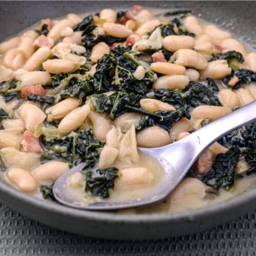A bowl of Tuscan Beans with pancetta and cavolo nero cabbage in a bowl with a spoon