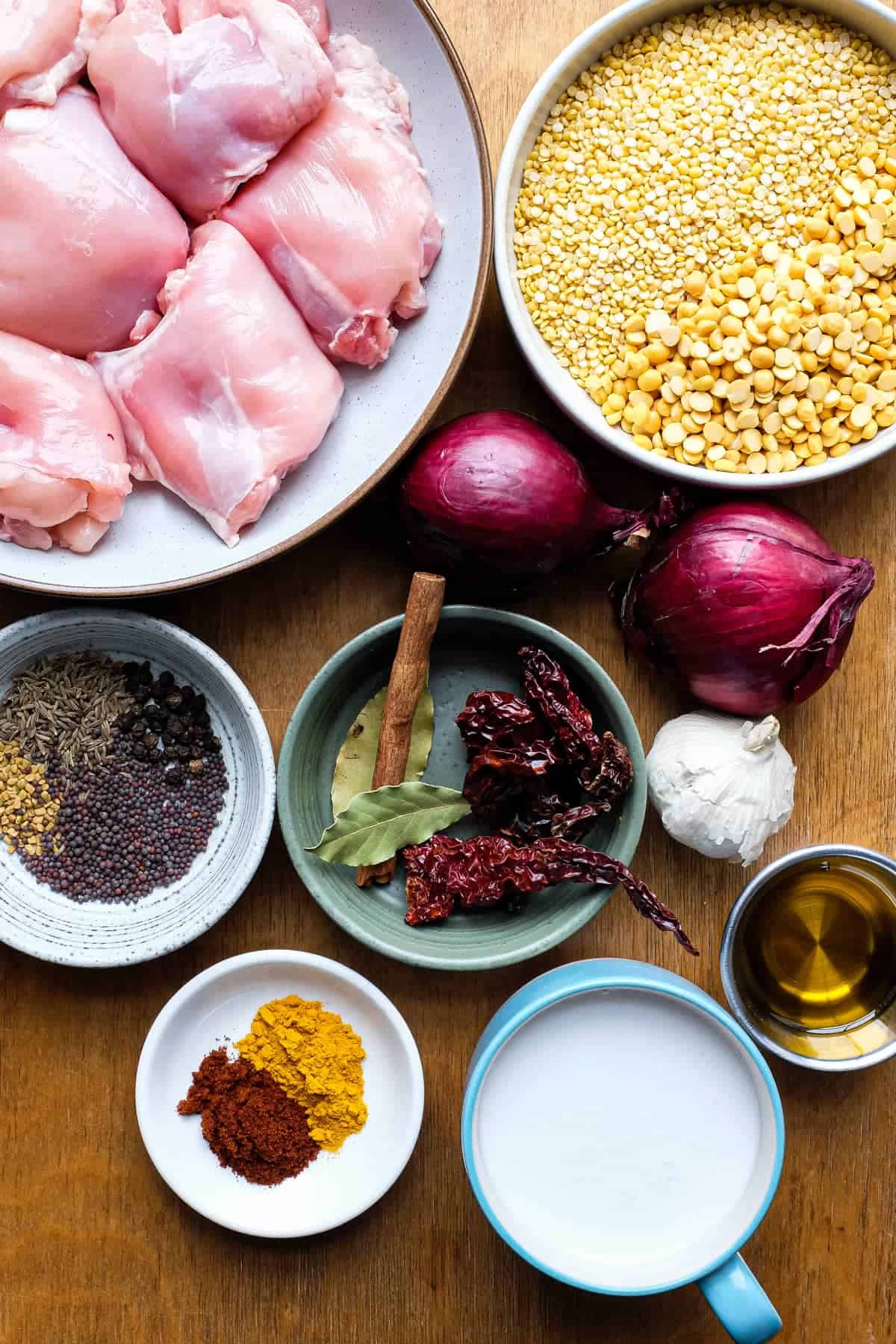 The ingredients for a chicken lentil curry including chicken, two types of lentils, onion, whole spices, ground spices, garlic, chillies and coconut milk