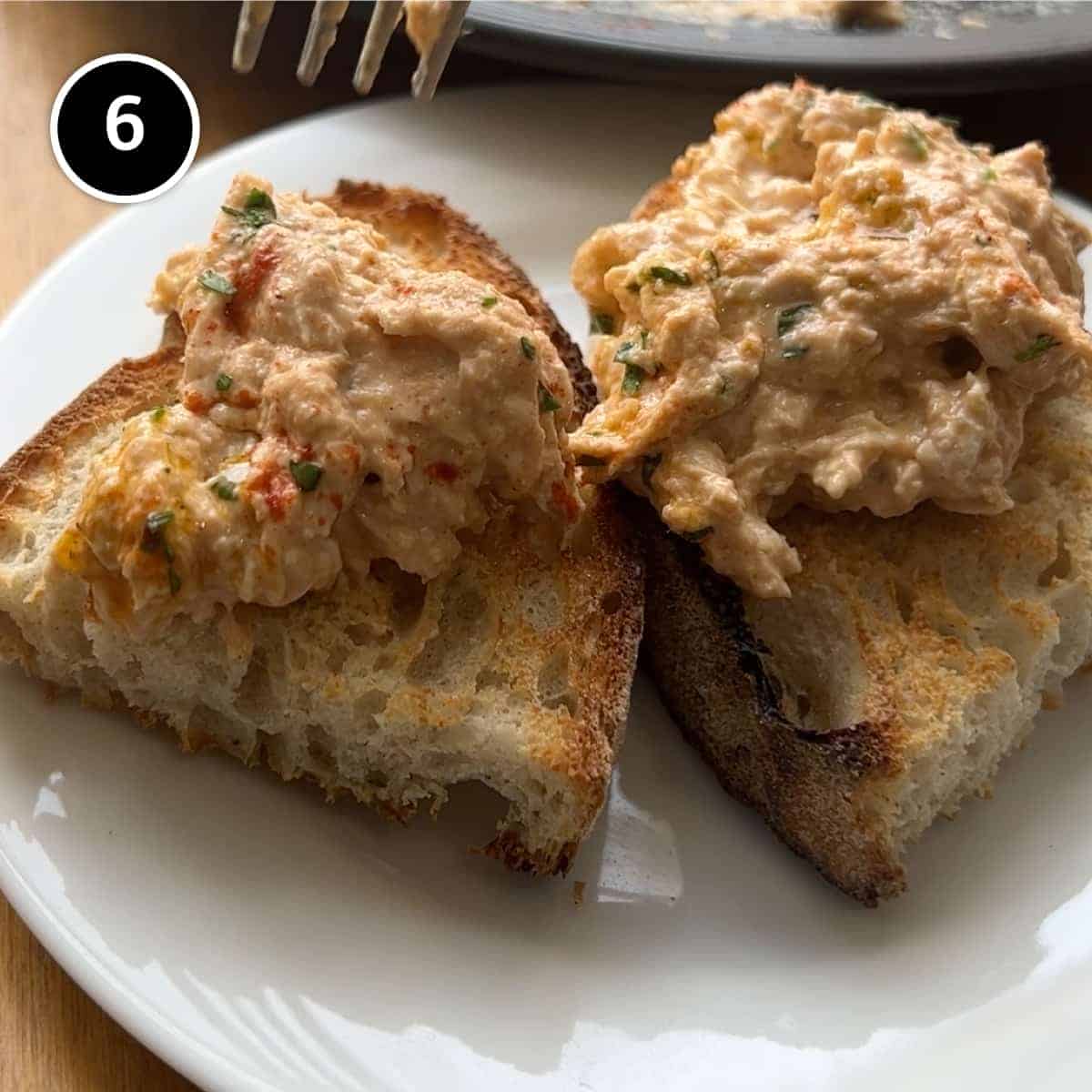 Two slices of toast with Circassian chicken. A platter. of Circassian chicken sits in the background