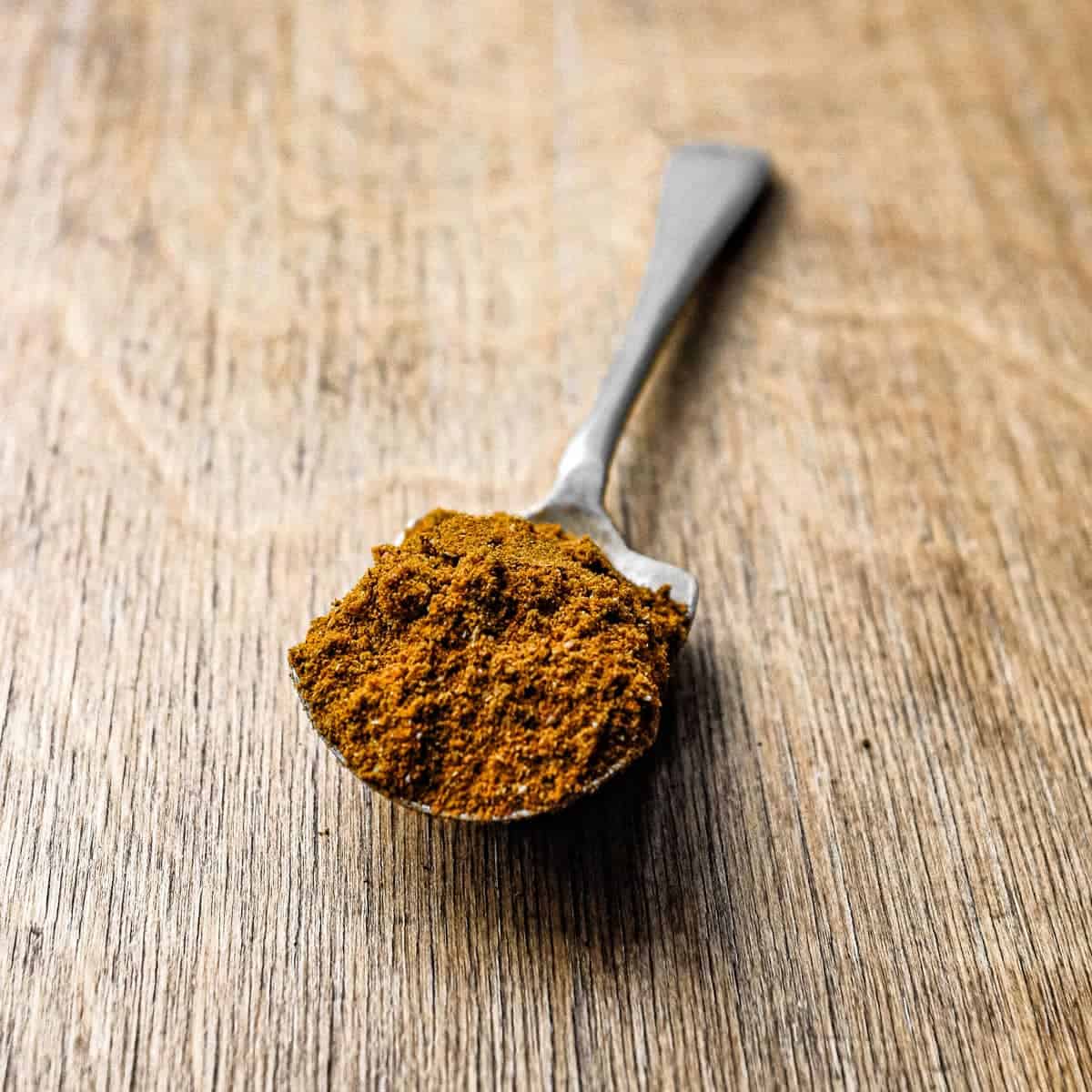 A teaspoon filled with Madras Curry Powder on a wooden surface