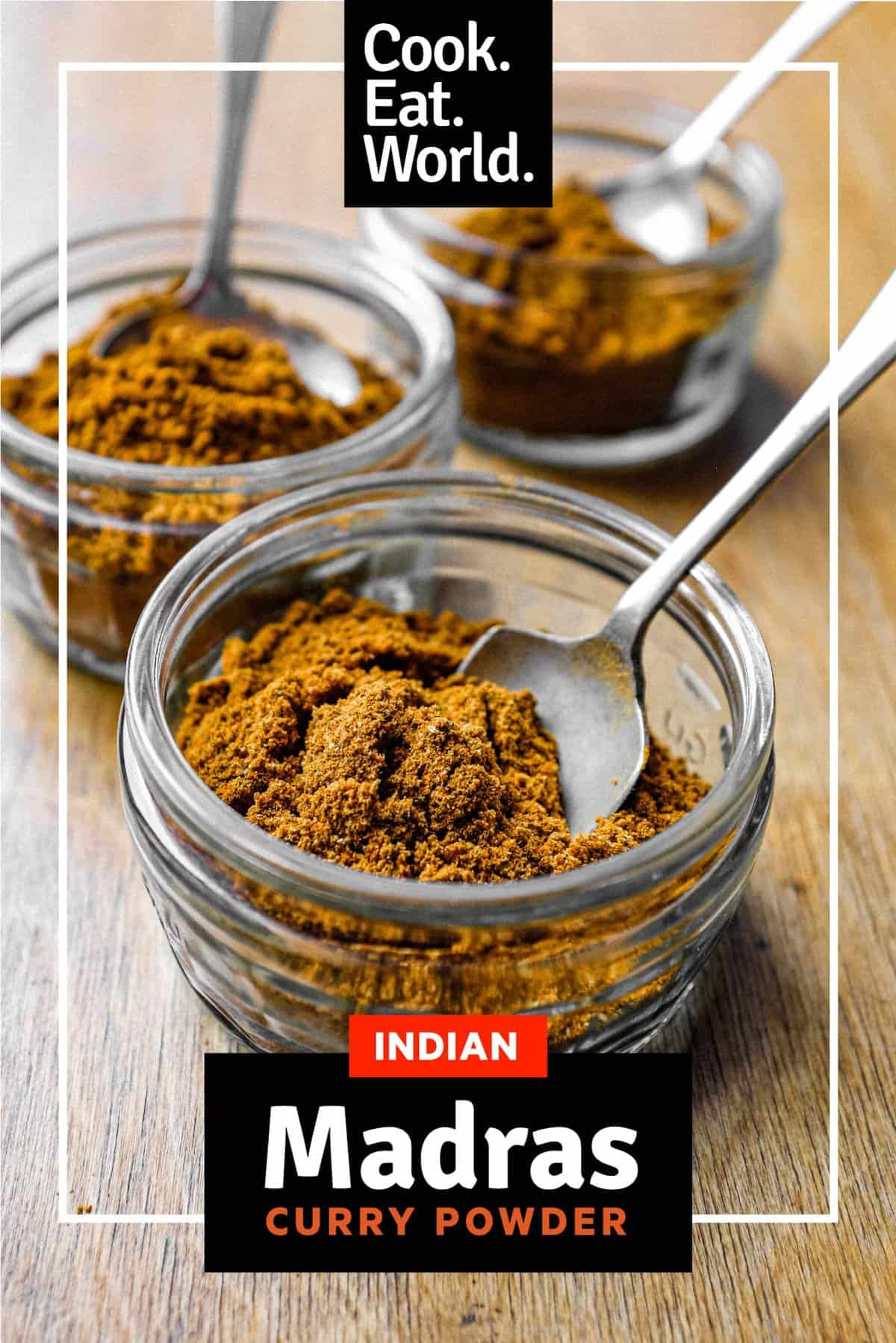 Three small jars of Madras curry powder with spoons on a wooden surface