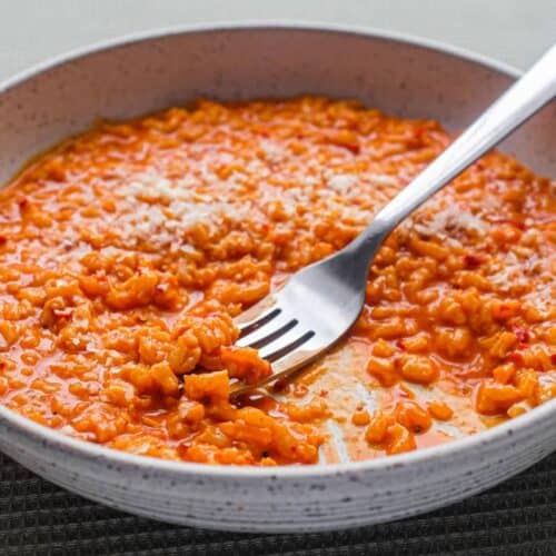 A bowl of Italian nduja risotto scattered with cheese. A fork sits alongside the bowl