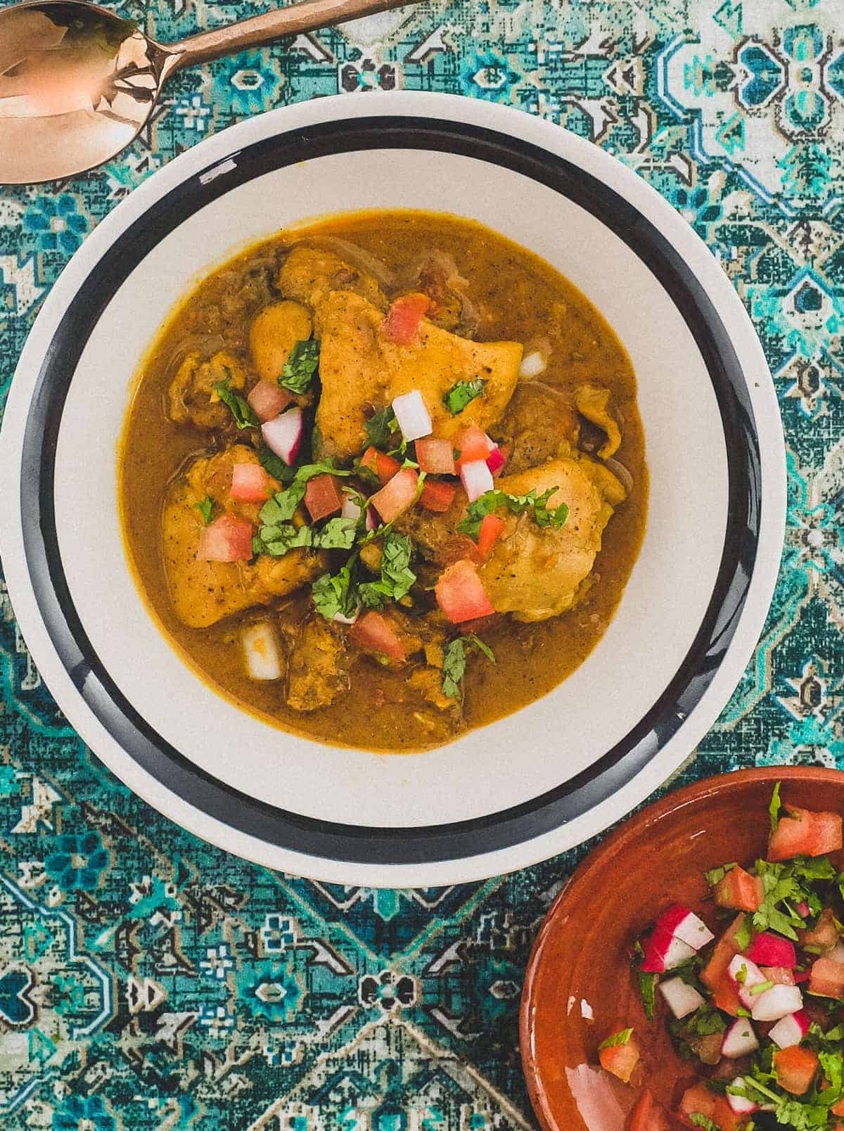 A bowl of Indian Black Pepper Chicken Curry with a side of tomatoes. A spoon sits alongside.