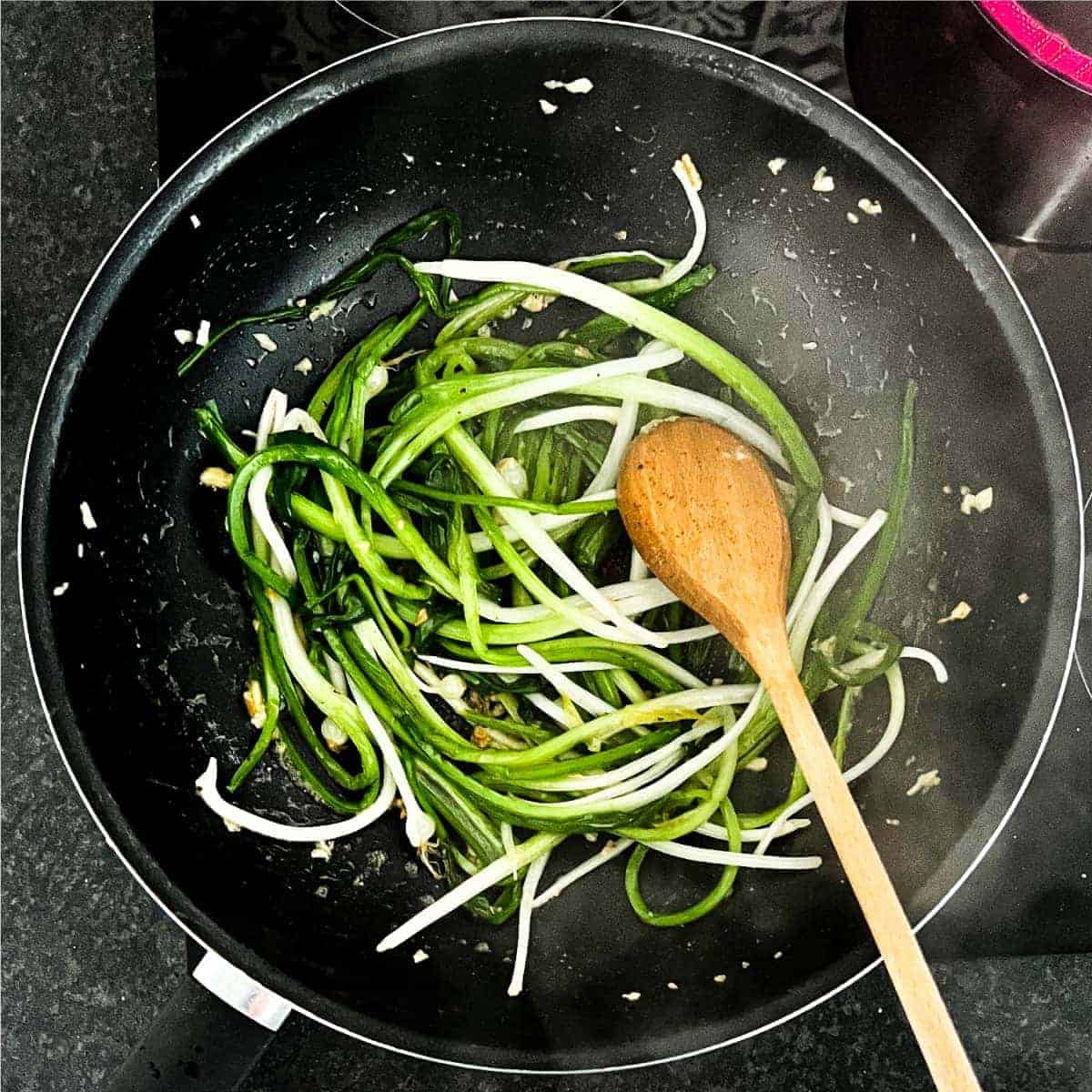 Wild onions frying in a pan with a wooden spoon