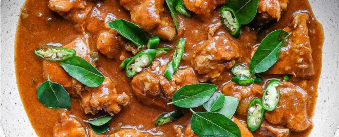 A bowl of Chicken Ceylon Curry scattered with fresh curry leaves and green chillies