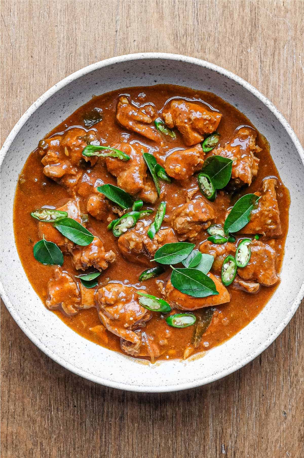 A bowl of Chicken Ceylon Curry scattered with fresh curry leaves and green chillies