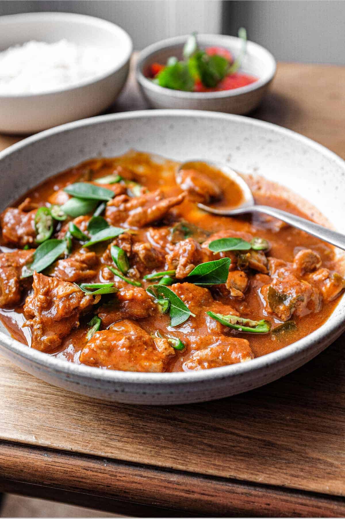 A bowl of Chicken Ceylon Curry scattered with fresh curry leaves and green chillies