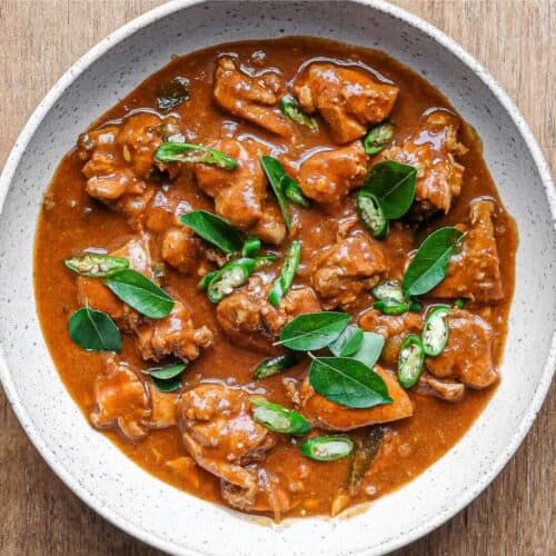 A bowl of Chicken Ceylon Curry scattered with fresh curry leaves and green chillies