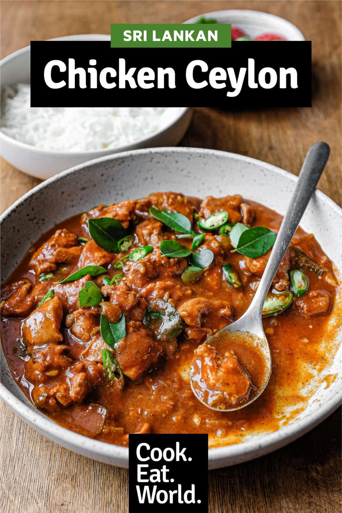 A bowl of Chicken Ceylon Curry scattered with fresh curry leaves and green chillies alongside a spoon