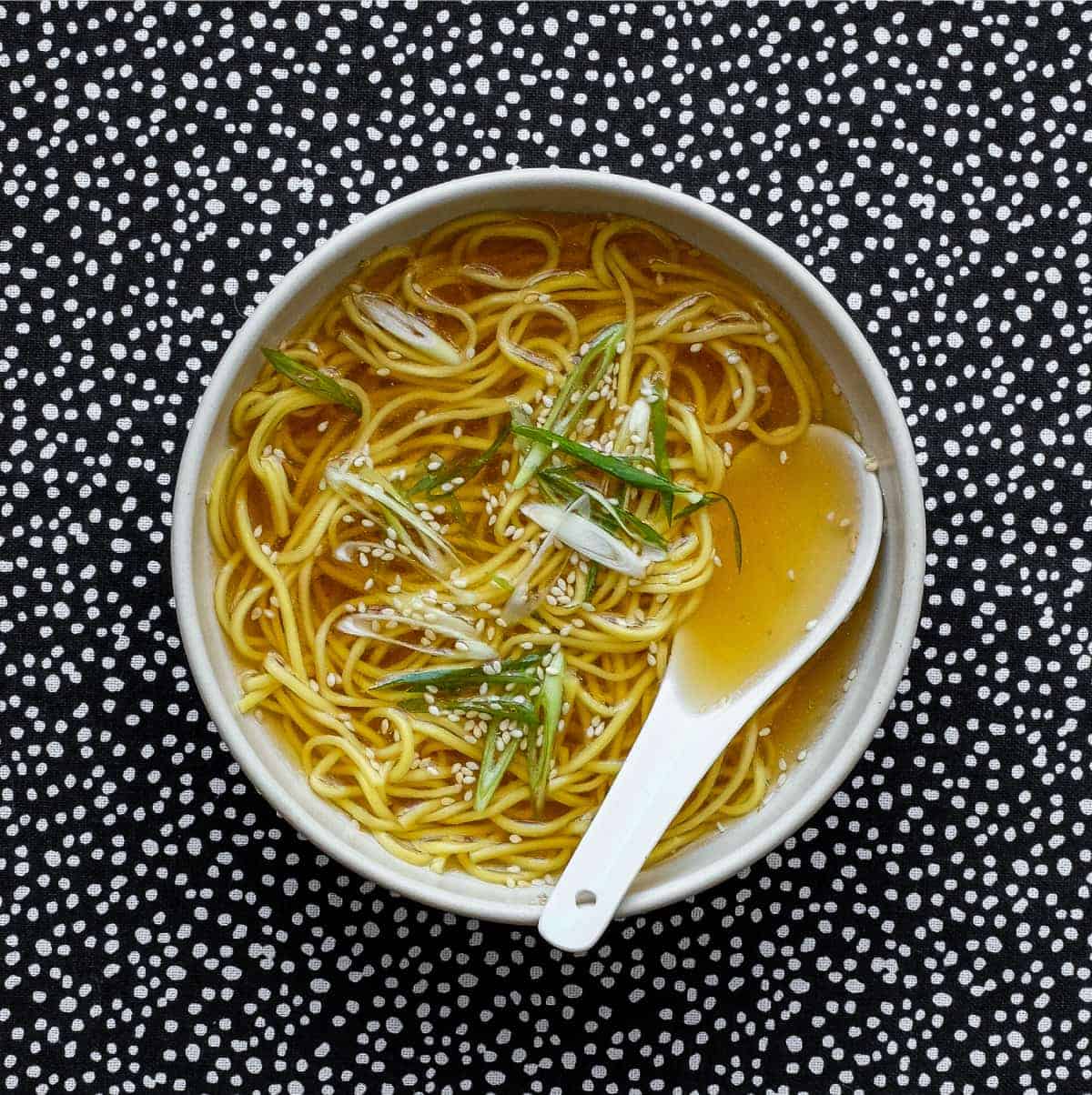 a small bowl of noodle soup sprinkled with sesame seeds and spring onion with a small china spoon