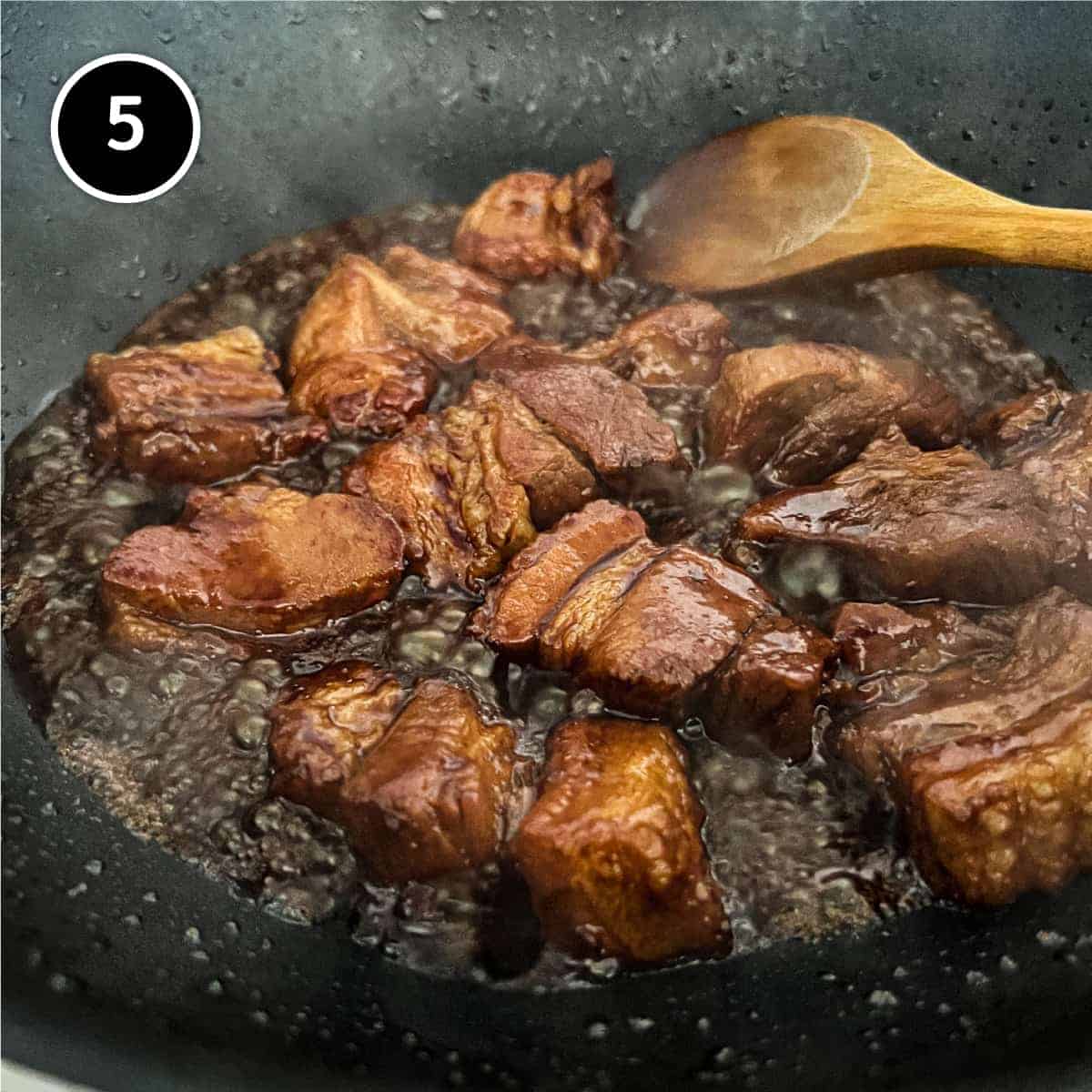 buta kakuni (pork) simmering in a deep brown simmering sauce along with a wooden spoon