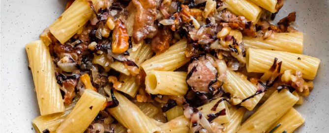 A bowl of rigatoni pasta with a radicchio, walnut and guanciale sauce in a bowl with a fork
