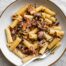 A bowl of rigatoni pasta with a radicchio, walnut and guanciale sauce in a bowl with a fork