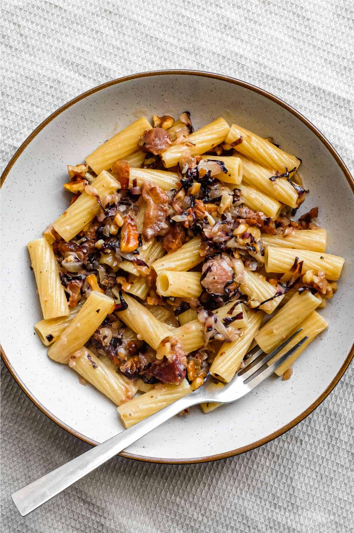 A bowl of rigatoni pasta with a radicchio, walnut and guanciale sauce in a bowl with a fork