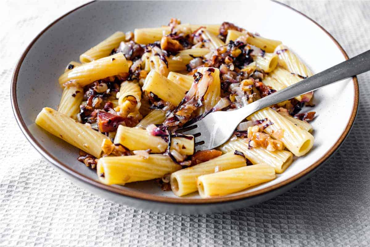 A bowl of rigatoni pasta with a radicchio, walnut and guanciale sauce in a bowl with a fork