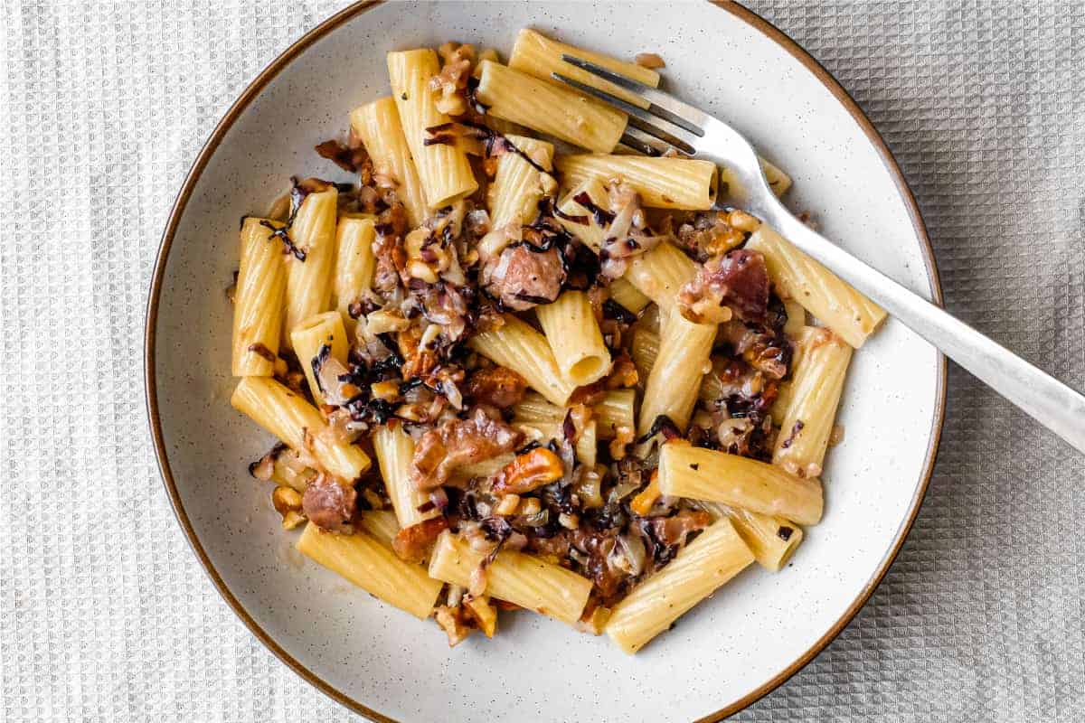 A bowl of rigatoni pasta with a radicchio, walnut and guanciale sauce in a bowl with a fork