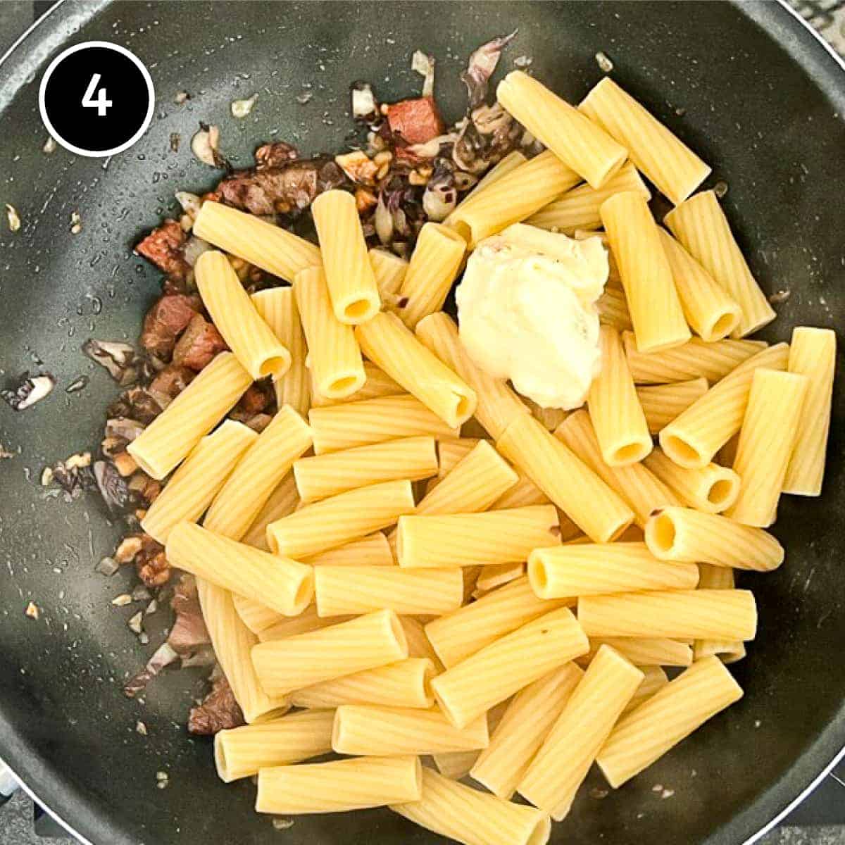 cooked rigatoni pasta is added to a radicchio sauce alongside a spoonful of gorgonzola cheese