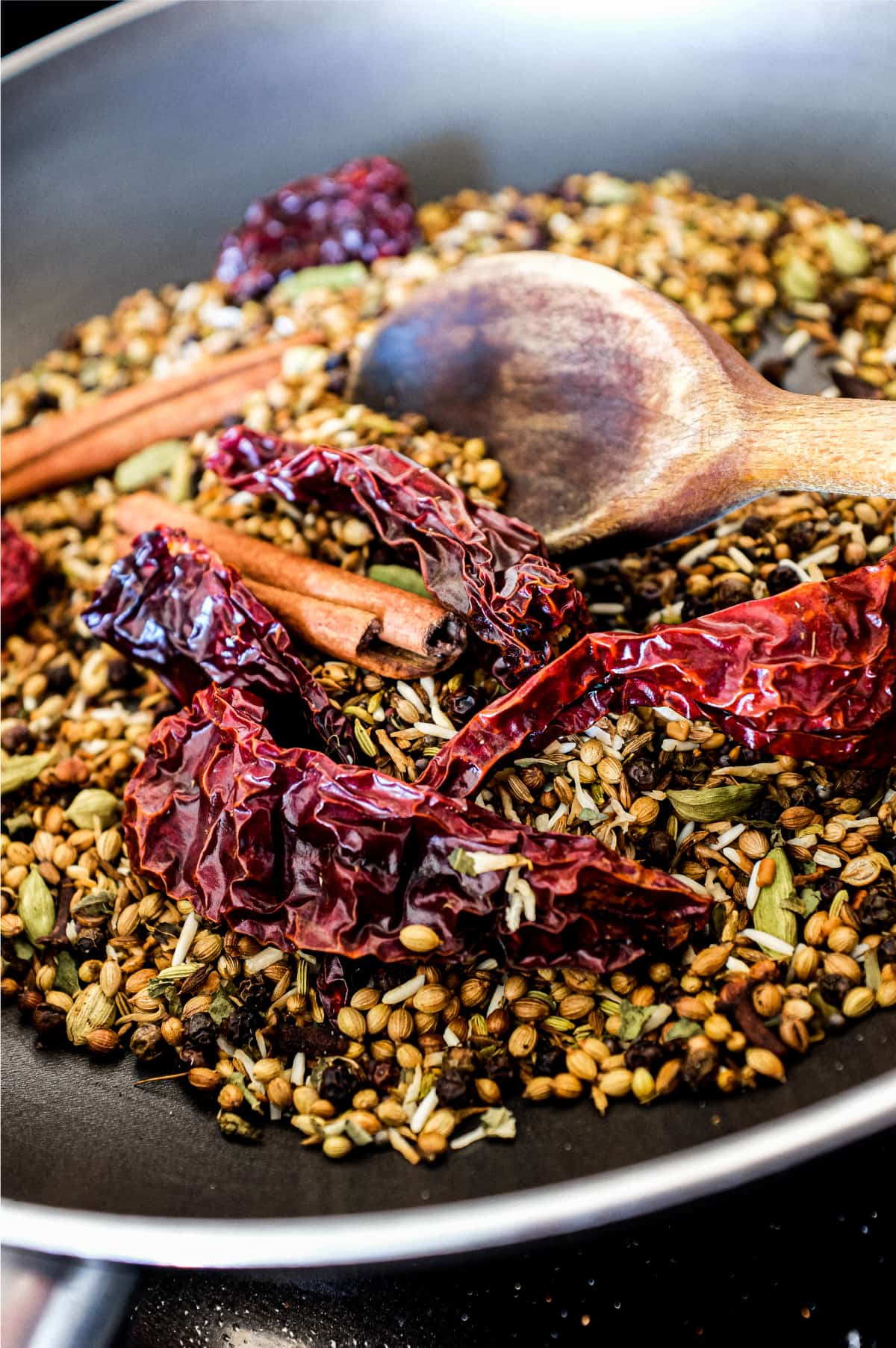 Whole spices dry frying in a pan with a wooden spoon