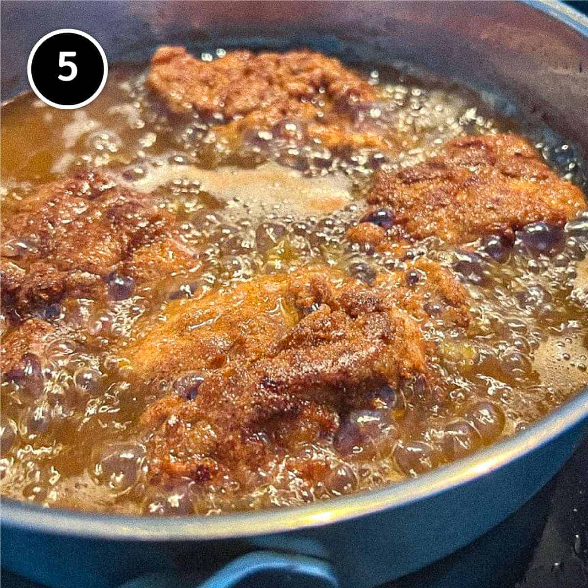 Chicken frying in a deep frying pan.