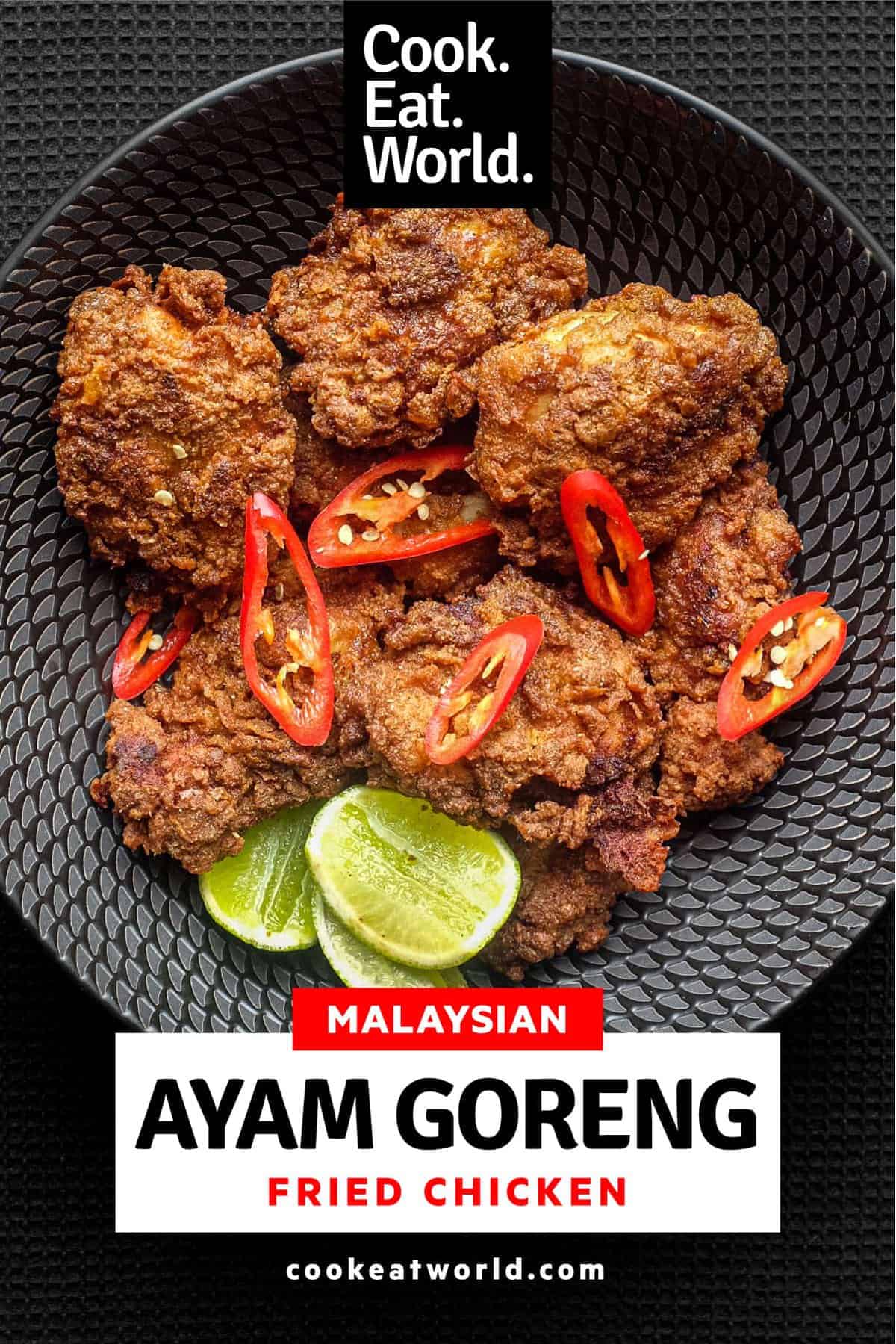 A black bowl filled with Malaysian fried chicken, Ayam Goreng, garnished with red chillies and accompanied by lime wedges.