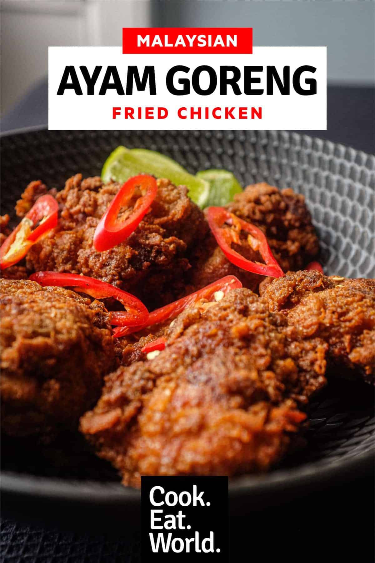 A black bowl filled with Malaysian fried chicken, Ayam Goreng, garnished with red chillies and accompanied by lime wedges.