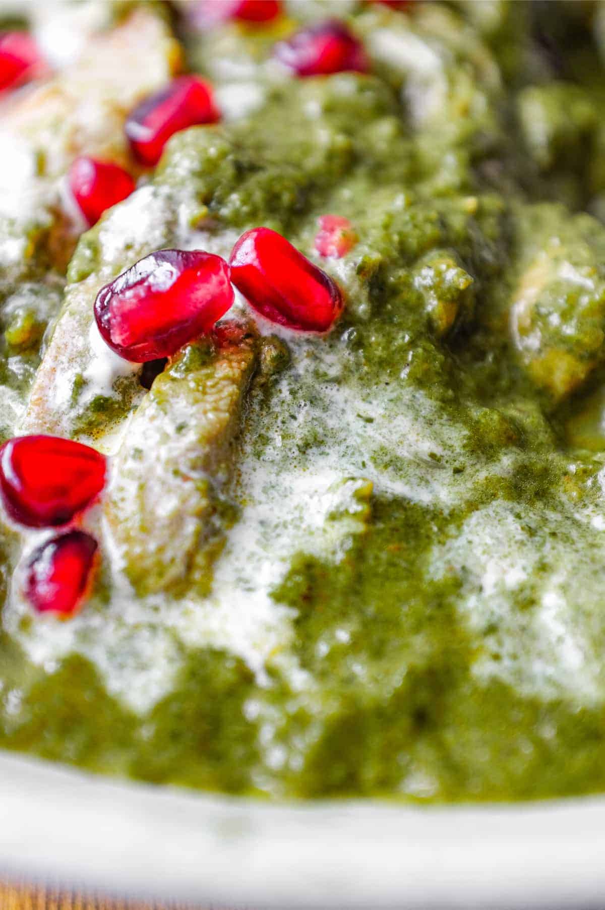 A bowl of Chicken Saag curry drizzled with fresh cream and sprinkled with pomegranate seeds.