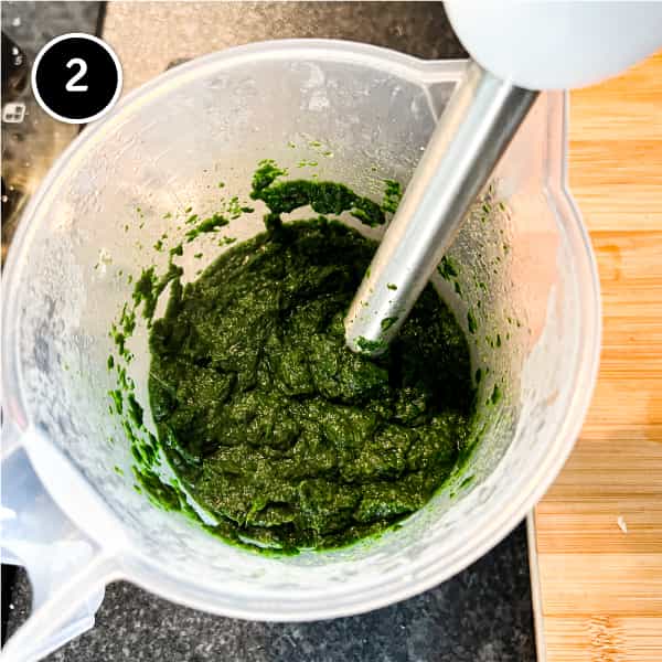 A stick blender creating a spinach puree from fresh spinach
