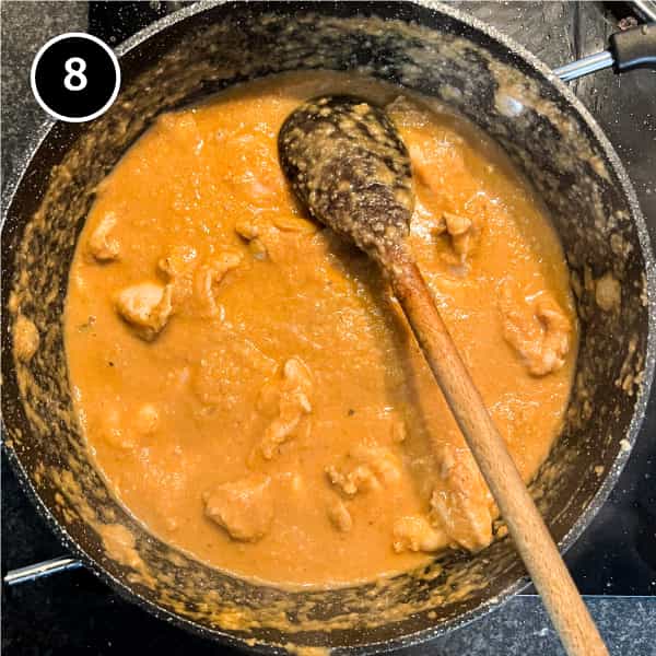 Chicken curry in a pan with a wooden spoon.