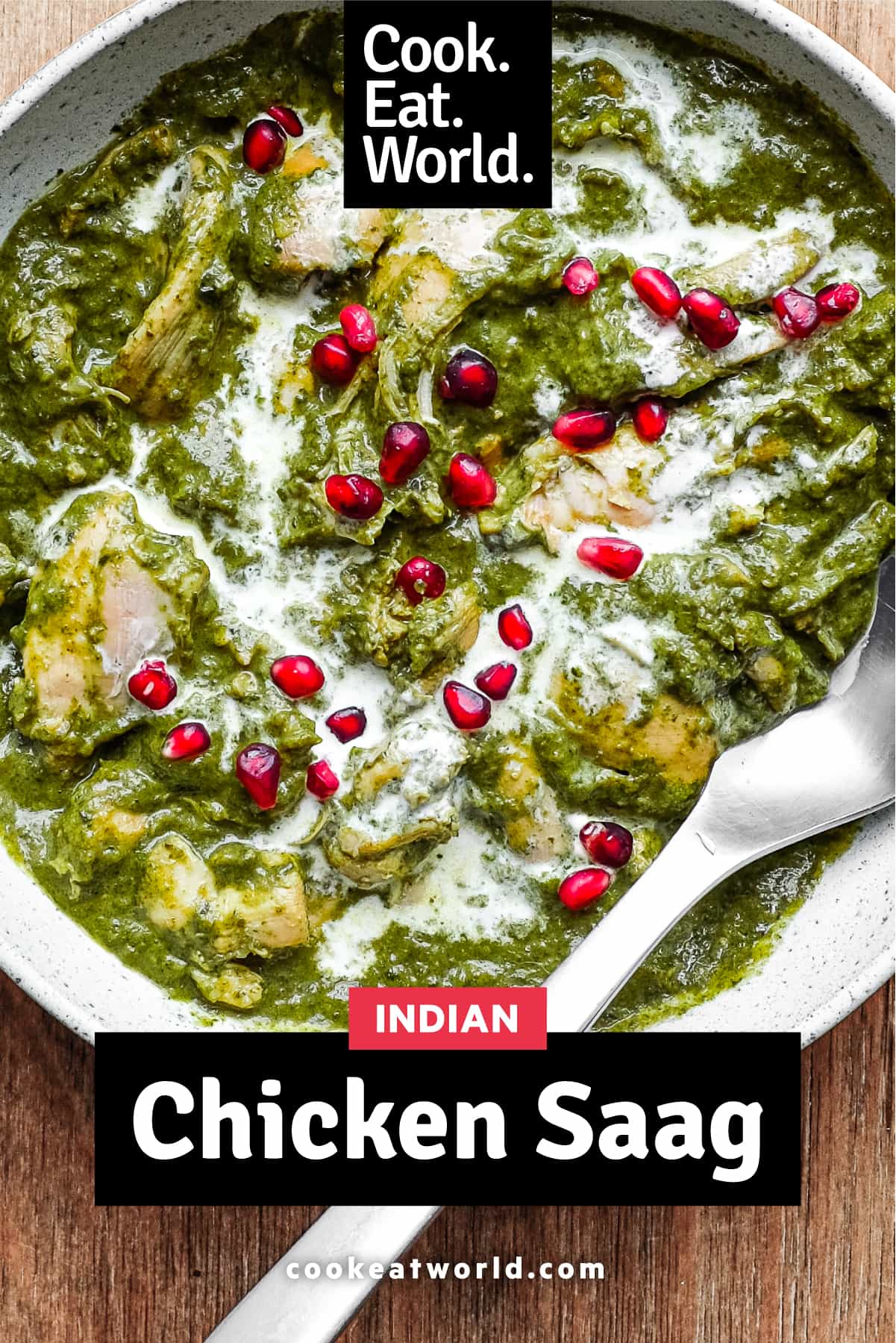 A bowl of Chicken Saag curry with a spoon, drizzled with fresh cream and sprinkled with pomegranate seeds.