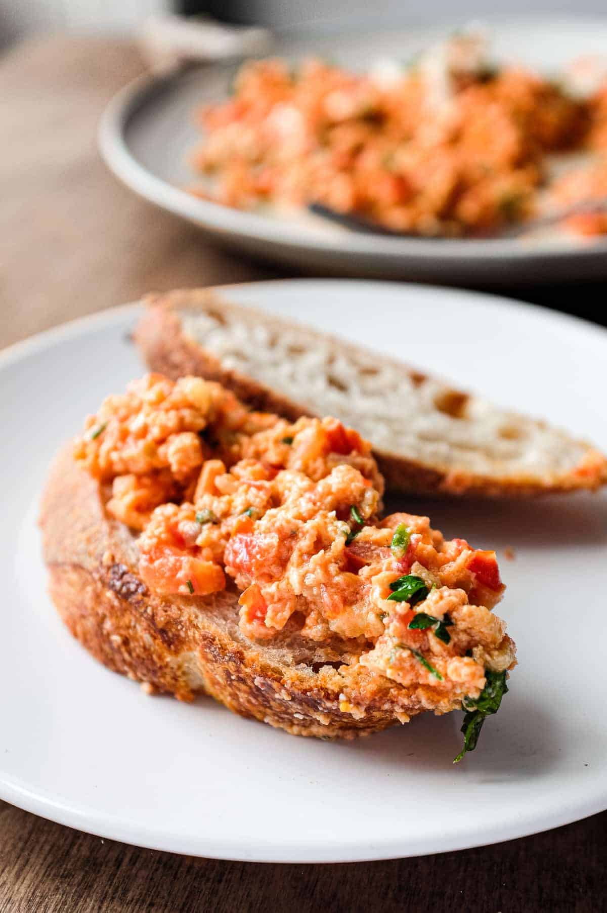 A plate of Greek Strapatsada scattered with feta cheese and parsley. Crusty bread and a fork sits alongside.