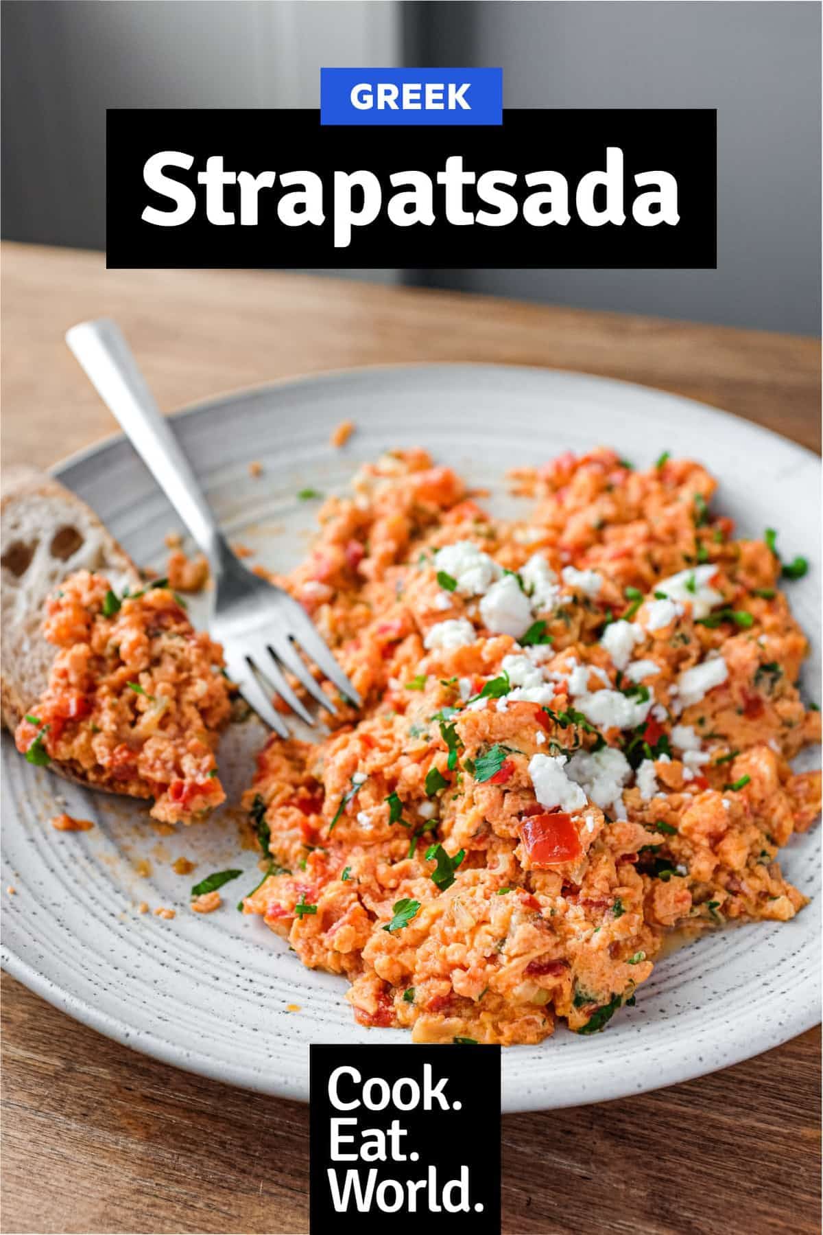 A plate of Greek Strapatsada scattered with feta cheese and parsley. Crusty bread and a fork sits alongside.