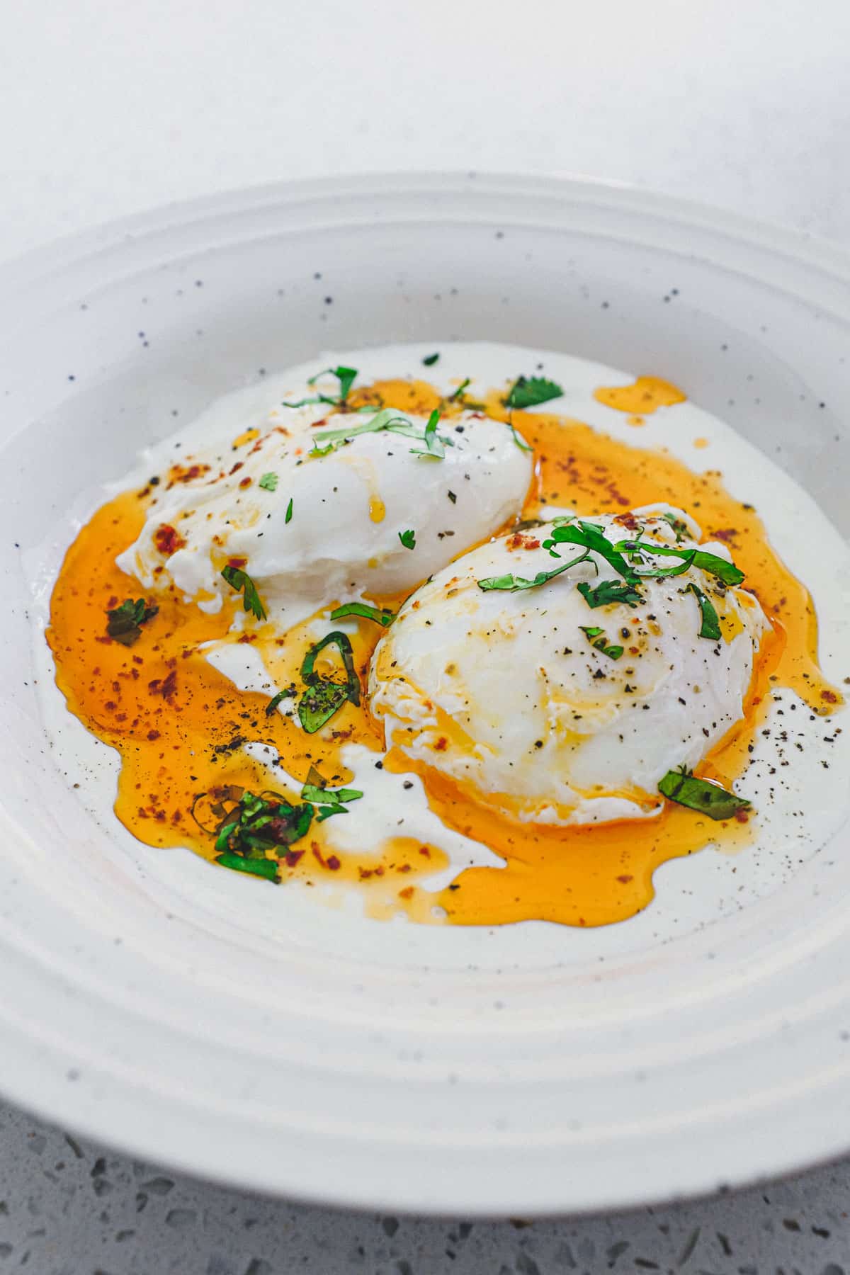 A small bowl of Turkish Cilbir (poached eggs) drizzled in orange Aleppo pepper butter