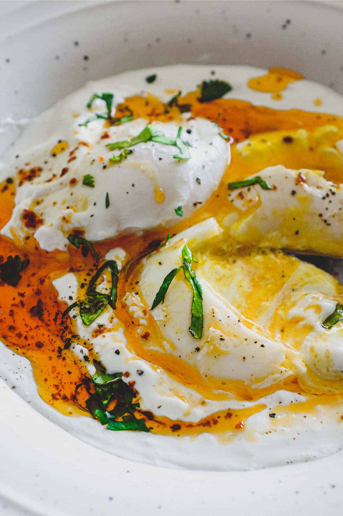 A small bowl of Turkish Cilbir (poached eggs) drizzled in orange Aleppo pepper butter